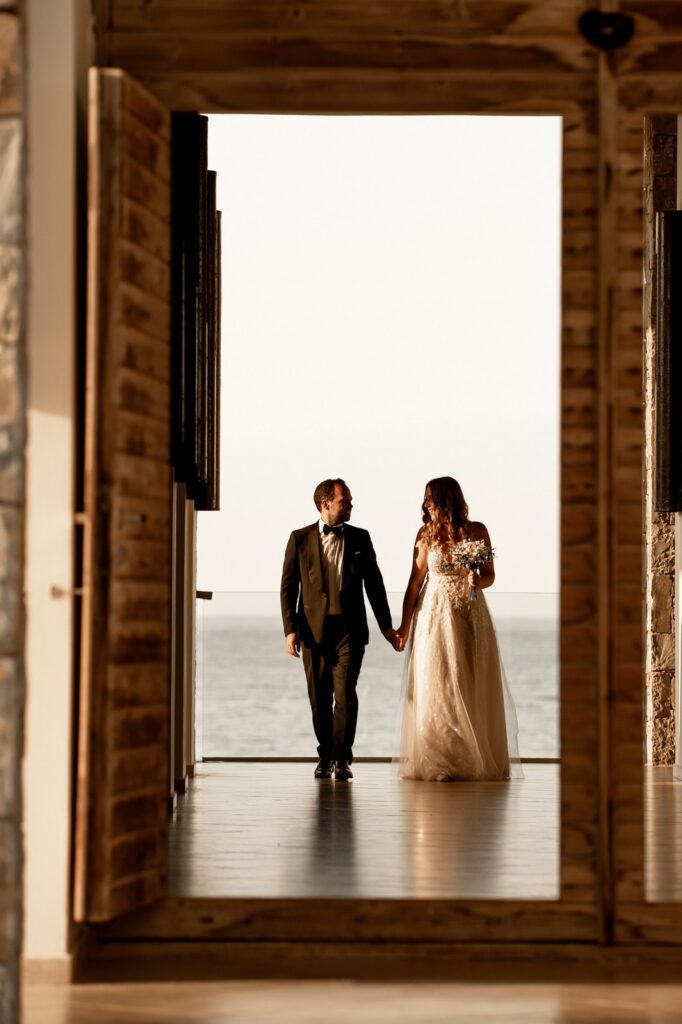 A shot of Theodore and Marie holding hands through a door, with the sea in the backround | Esthesis Events