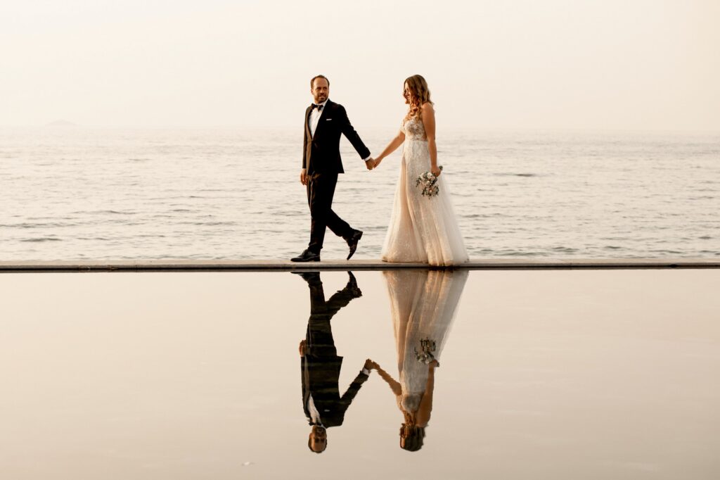 Theodore and Marie holding hands poolside with the sea in the backround | Esthesis Events