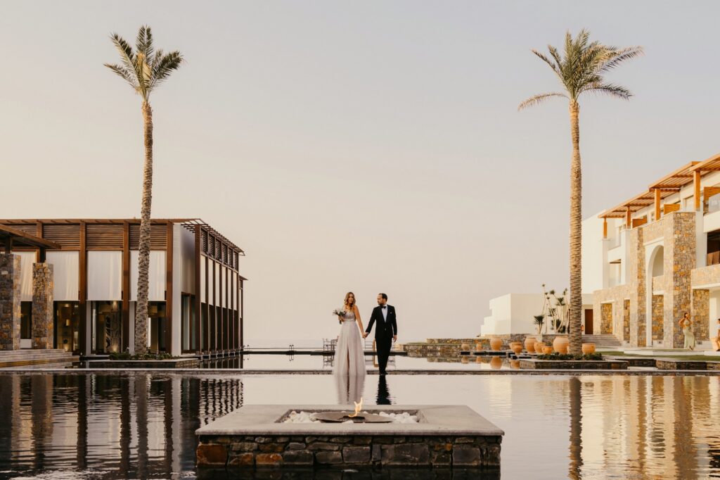 Marie and Theodore posing poolside under the palm trees at Kipos Aisthiseon | Esthesis Events