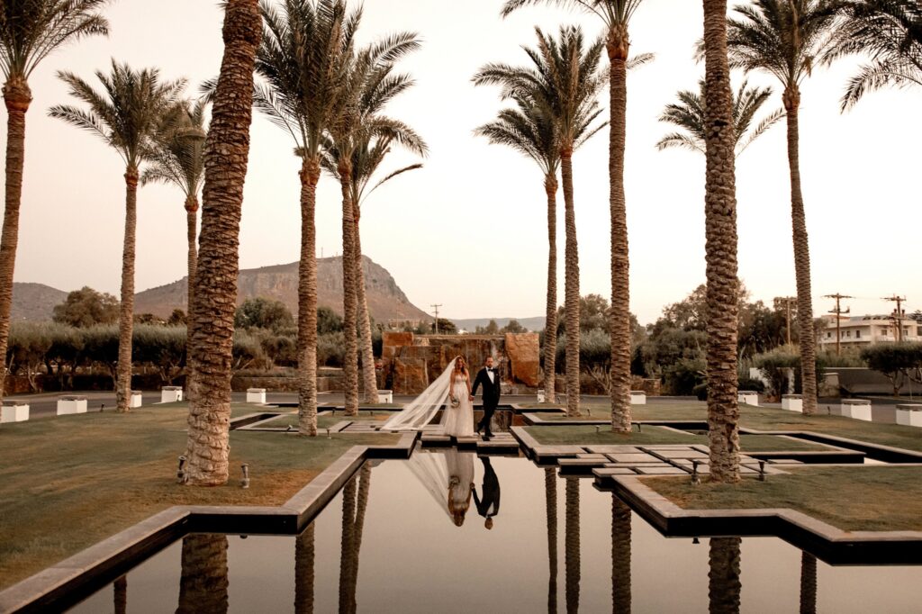 Marie and Theodore posing poolside under the palm trees at Kipos Aisthiseon | Esthesis Events