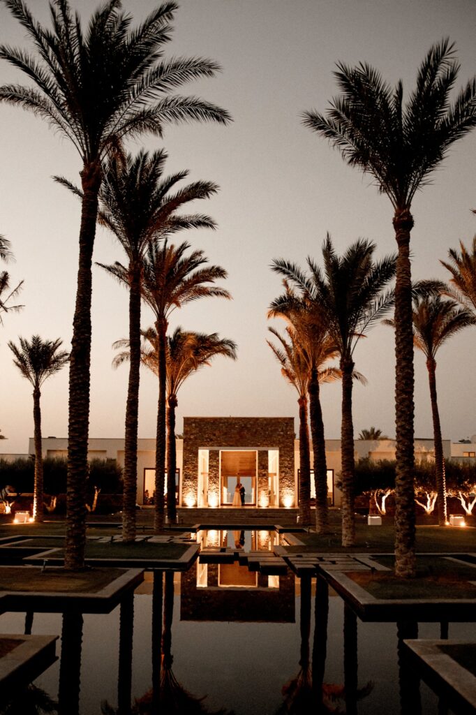 An evening shot of the pool and palm trees of Kipos Aisthiseon, with Marie and Theodore in the backround | Esthesis Events