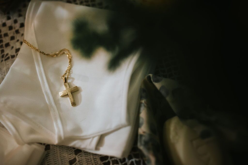 A gold cross necklace and a white garment related to a baptism ceremony | Esthesis Events A gold cross necklace and a white garment related to a baptism ceremony | Esthesis Events