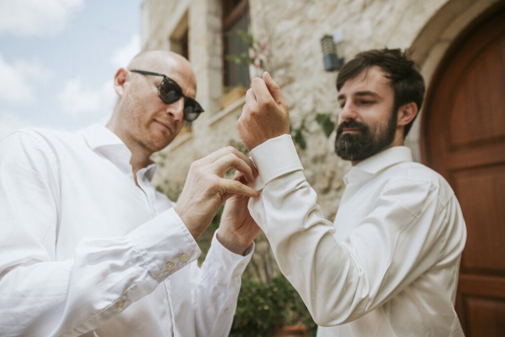 A groomsman helping Michael fasten his cufflinks before the wedding. | Esthesis Events A groomsman helping Michael fasten his cufflinks before the wedding. | Esthesis Events
