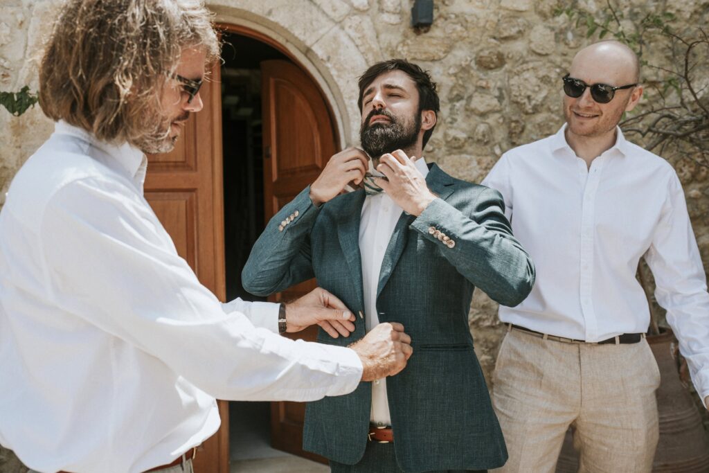 Michael fixing his bow tie as a groomsman helps adjust his jacket. | Esthesis Events Michael fixing his bow tie as a groomsman helps adjust his jacket. | Esthesis Events