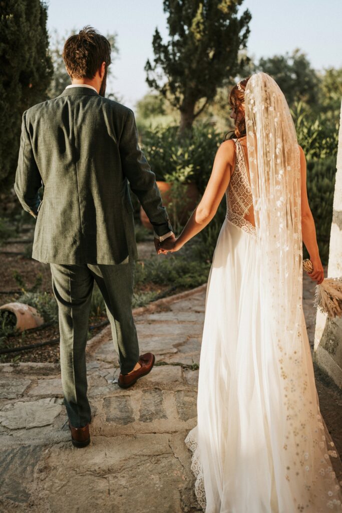 The newlyweds walking hand-in-hand, captured from behind as they move together. | Esthesis Events The newlyweds walking hand-in-hand, captured from behind as they move together. | Esthesis Events