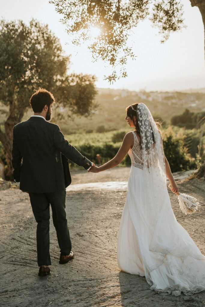 The newlyweds walking hand-in-hand, captured from behind as they move together. | Esthesis Events The newlyweds walking hand-in-hand, captured from behind as they move together. | Esthesis Events