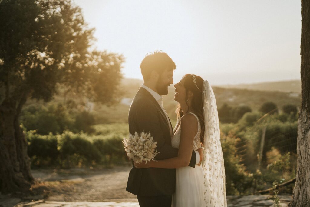 An intimate, sunlit close-up of the newlyweds sharing a warm smile and locking eyes in the olive garden at Agreco Farm. | Esthesis Events An intimate, sunlit close-up of the newlyweds sharing a warm smile and locking eyes in the olive garden at Agreco Farm. | Esthesis Events