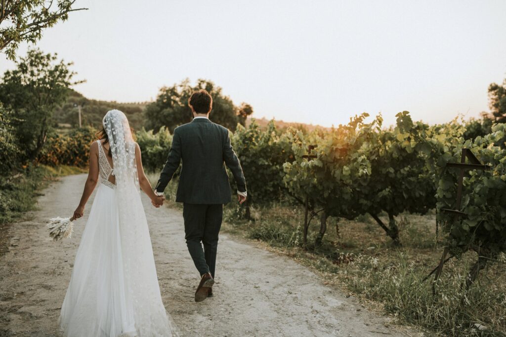 The newlyweds captured from behind as they stroll hand-in-hand through the scenic Agreco Farm vineyard. | Esthesis Events The newlyweds captured from behind as they stroll hand-in-hand through the scenic Agreco Farm vineyard. | Esthesis Events