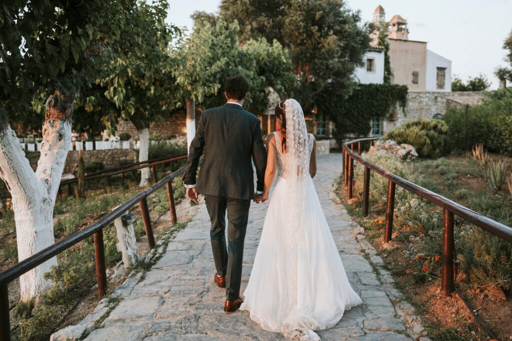 A view from behind of Michael and Jodie walking hand-in-hand down a stone path at Agreco Farm. | Esthesis Events A view from behind of Michael and Jodie walking hand-in-hand down a stone path at Agreco Farm. | Esthesis Events